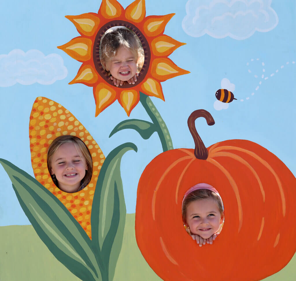 Four-year-old Acton twins Sophie Carlucci, lower right, and Lucy Carlucci, lower left, and sister Chloe Carlucci, 2, top, try out the new Ag Day face-in-the-hole board.
