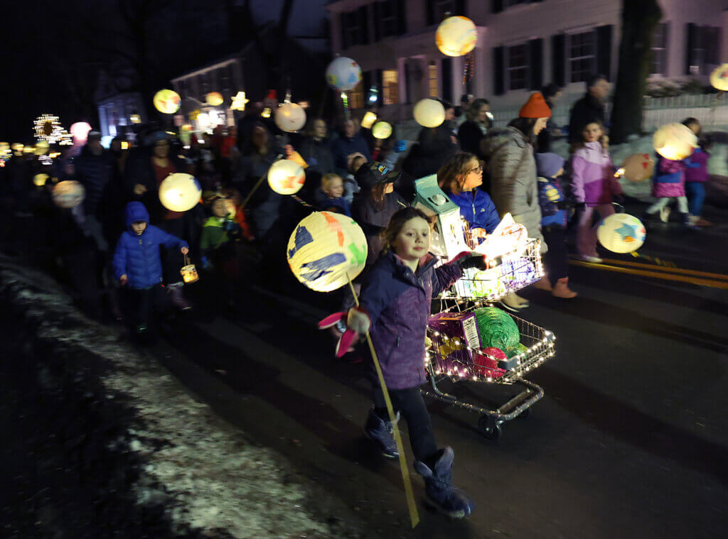 Children push a shopping cart lantern, sponsored by Debra’s Natural Gourmet and the work of several Art for All artists, through Acton Center. 