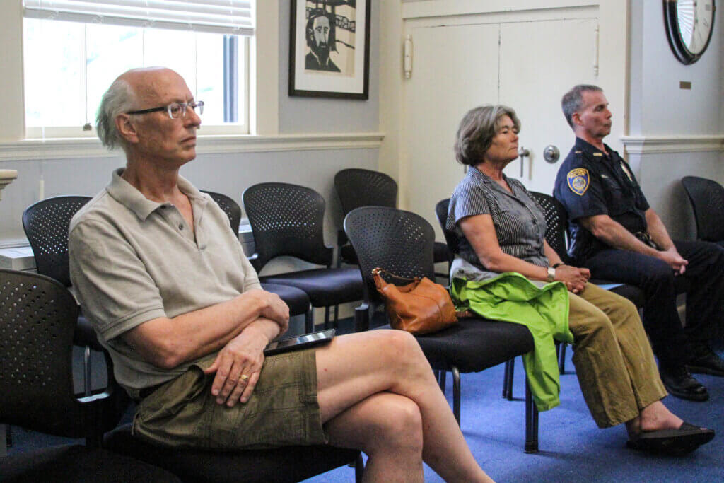 Read, left, waits for a Select Board meeting to begin with town Natural Resources Director Delia Kaye and Acton police Capt. Brian Goldman also in the audience. Photo: Dakota Antelman/The Acton Bridge