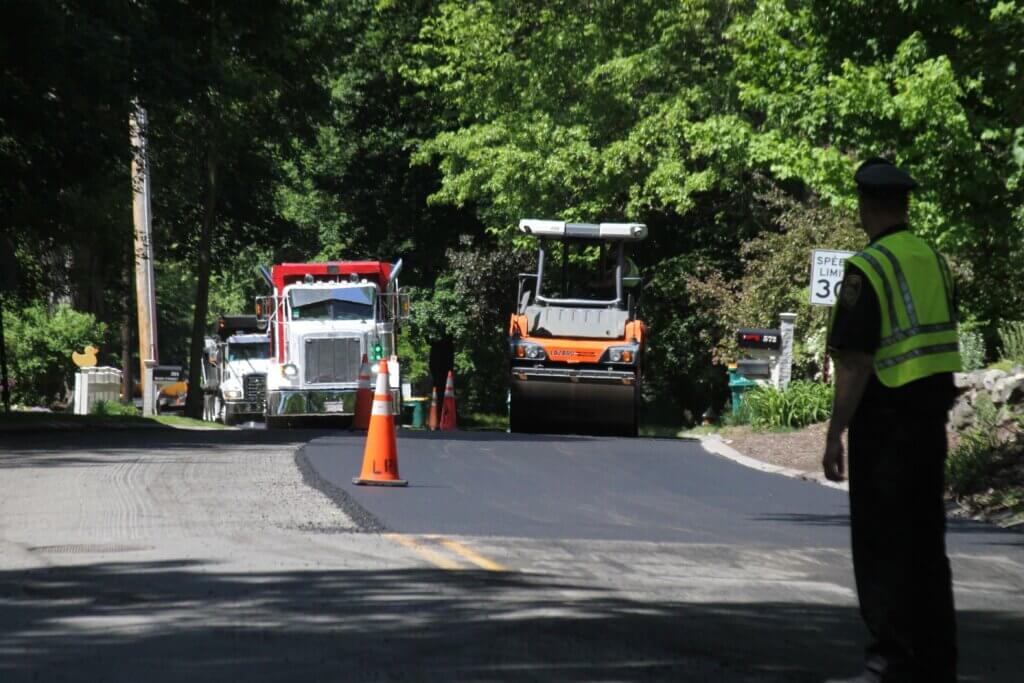 An officer stands watch as crews tamp down new Main Street pavement. Photo: Dakota Antelman/The Acton Bridge