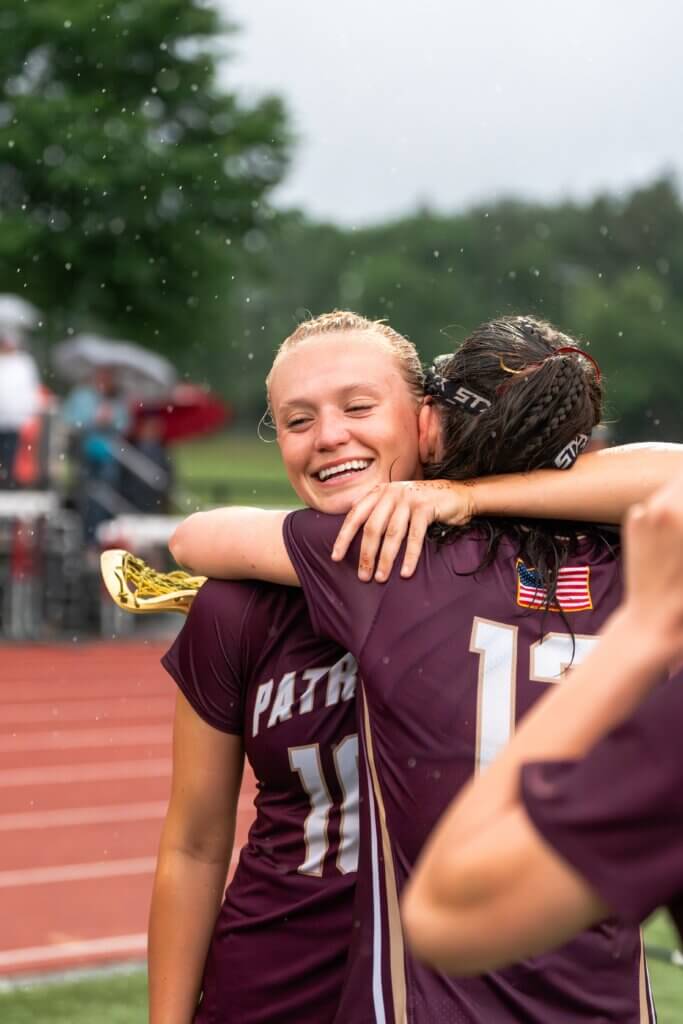 Lindsay Cain (left) hugs a teammate after the Pats edged Chelmsford, 6-5, in the rain to advance to the state championship game. Photo by Aidan Moroney
