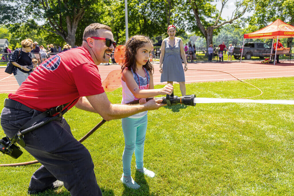 Acton Firefighter Evan Foisey offers Aria Licciarda some guidance as Aria’s mom, Rayna, looks on. Photo: Stephen Beyer/The Acton Bridge