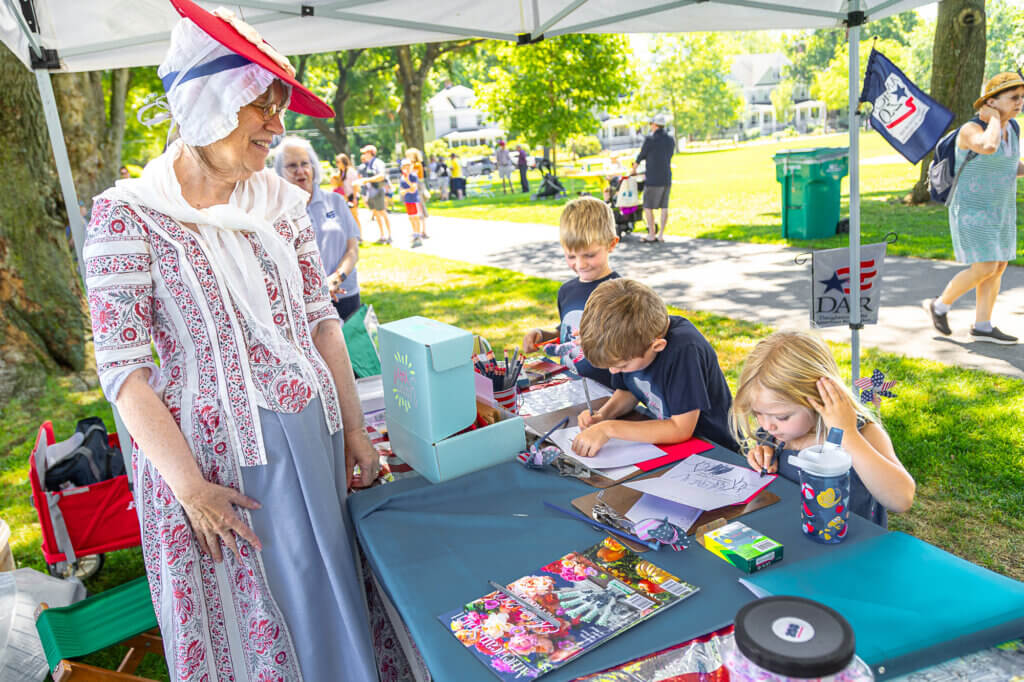 At the Daughters of the American Revolution booth, Alice Galinat helps children make cards that will be mailed to veterans to thank them for their service. Photo: Stephen Beyer/The Acton Bridge