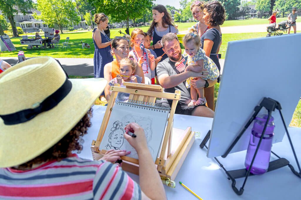 Sam and Ronan Dunne sit with children Cara, 4, and Eabha, 1, while Acton caricaturist Samara Reid sketch them. Photo: Stephen Beyer/The Acton Bridge