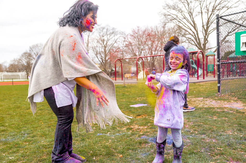 Rose Cratsley and her daughter Arya smile from beneath a dusting of the colored powders used to celebrate the Hindu holiday of Holi. Photo: Stephen Beyer/The Acton Bridge