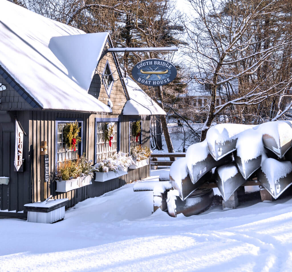 Stacked watercraft wait silently beneath the snow outside The South Bridge Boathouse. Photo by Stephen Beyer