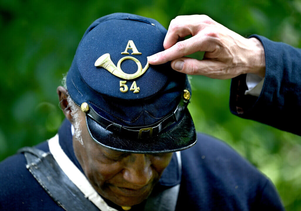 Morgan Kuberry, portraying a Union lieutenant, points to insignia showing a bugle for infantry from the 54th Massachusetts Volunteer Infantry, Company A, on the top of re-enactor Joe Zellner’s cap during a living history presentation at the Robbins House in Acton on Saturday, July 26, 2025. Ken McGagh/The Acton Bridge