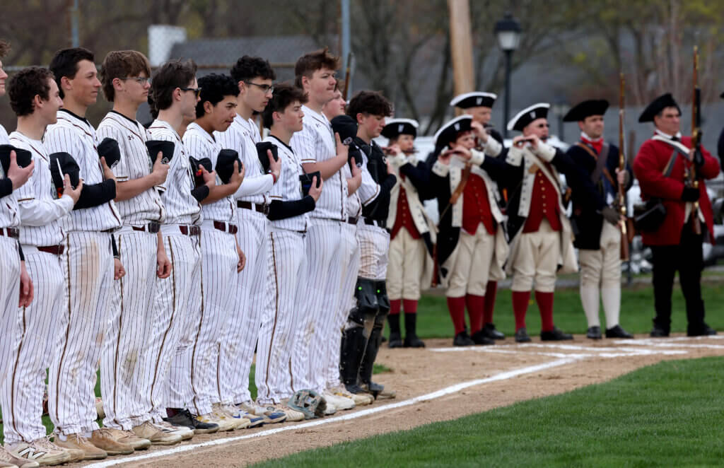 The Acton-Carlisle baseball team stands as the Acton Minute Men fife and drum corps plays the national anthem. Photo: Ken McGagh/The Acton Bridge
