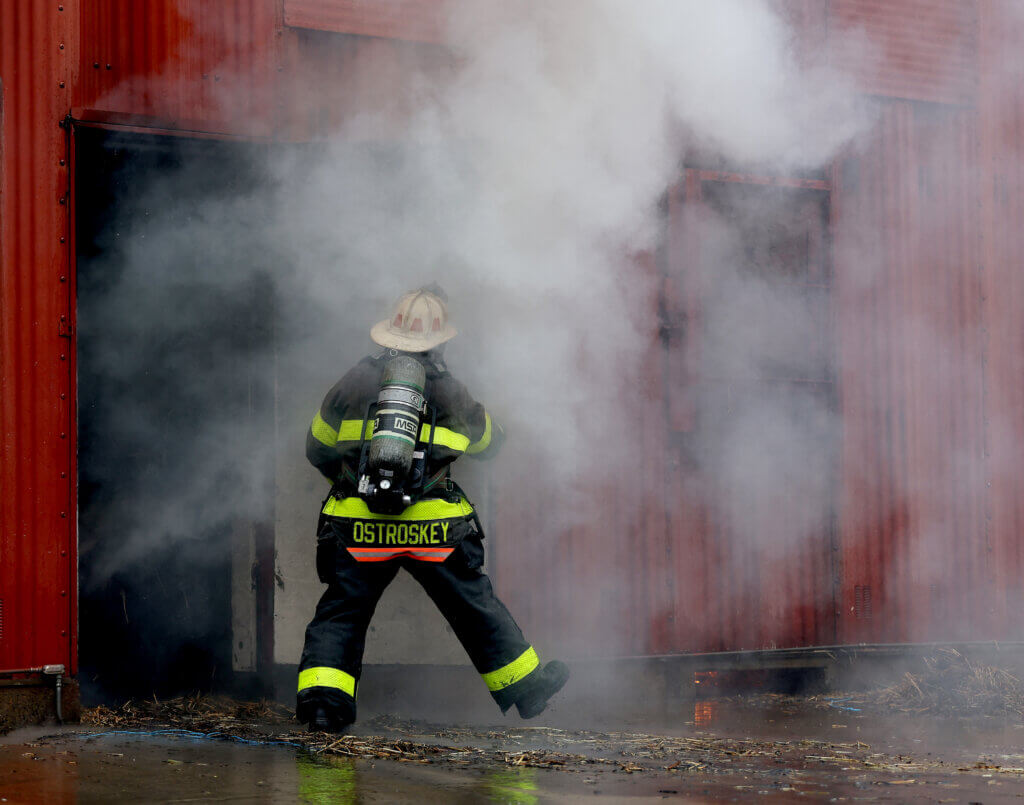 Smoke pours from the Worcester Fire Department Training Center’s burn building as Acton firefigher Rachel Vroegindewey emerges during a “refresher” training session on Monday, September 27, 2026. This week was the first time Acton firefighters have trained at the Worcester facility. Ken McGagh/The Acton Bridge