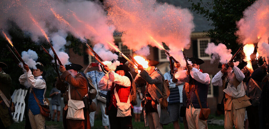 Revolutionary War re-enactors from the Acton Minute Men, Acton Minutemen, and 6th Middlesex Regiment fire a musket volley during Concord250’s “250 Days to the 250th: Community Kickoff” on August 11. Photo: Ken McGagh/The Acton Bridge
