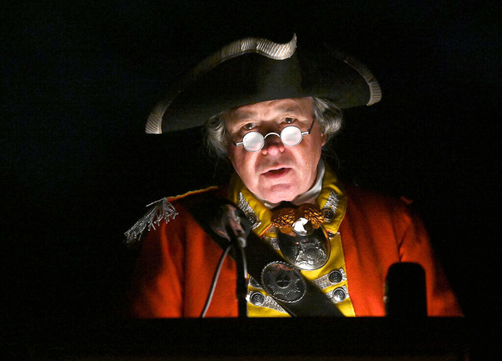Portraying a British officer in the 10th Regiment of Foot, Paul O’Shaughnessy recites the names of British war dead during the seventh annual Patriot Vigil at Minute Man National Historical Park on April 18, 2024. Photo: Ken McGagh/The Acton Bridge  