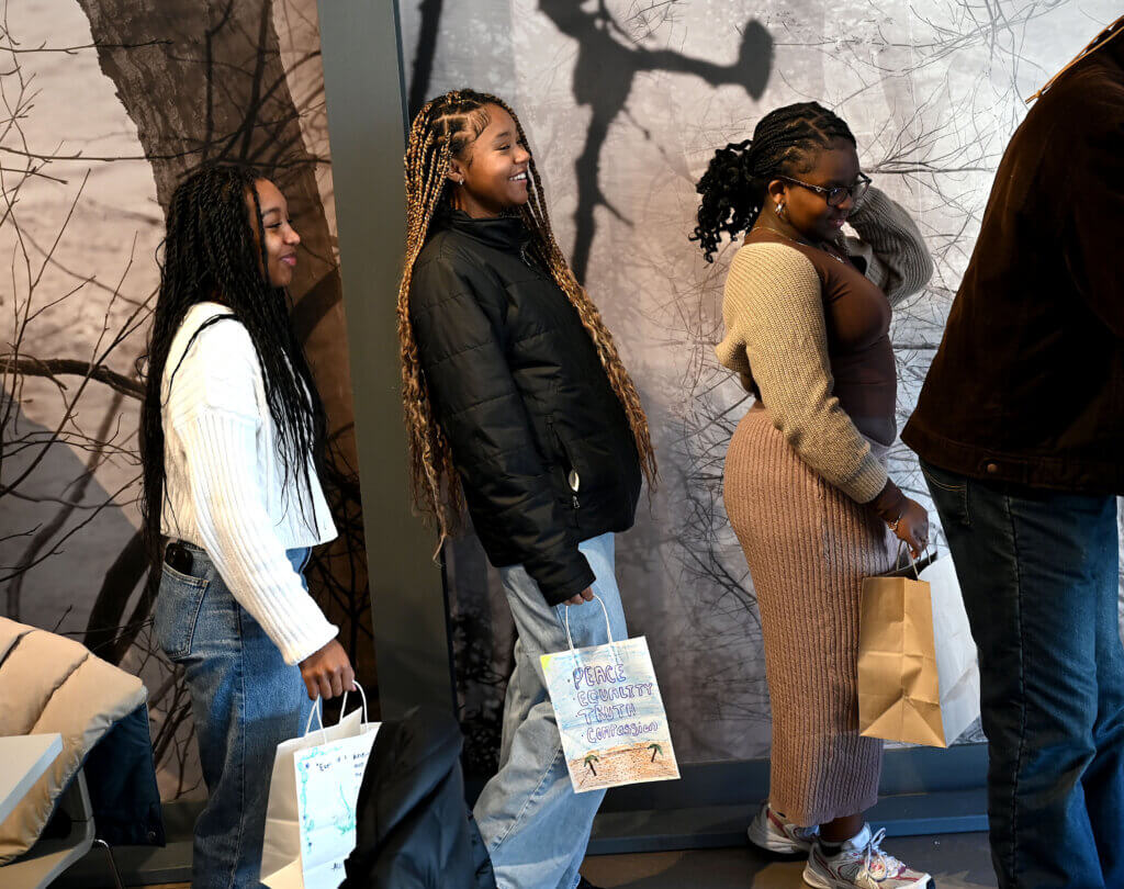 Acton Academy freshmen Melissa Asare, left, Ray’Hannah Mendez and Avery Barkley wait in line to fill a bag of food for local children at the Acton Museum on Monday, January 20, 2025. The Martin Luther King Day of Service activity was hosted by the Acton Museum Contemporary Leaders in partnership with Open Table. Ken McGagh/The Acton Bridge