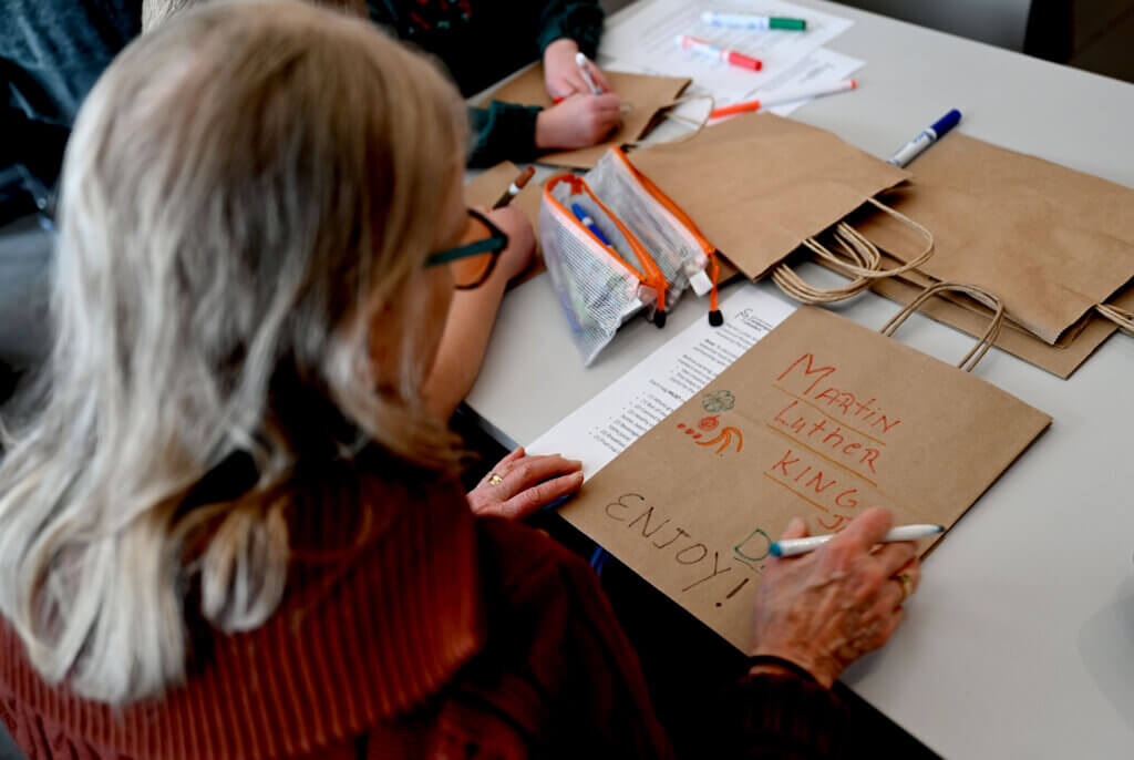 Kathy Hassinger of Newton, a grandparent of Henry and Audrey Hassinger of Acton, decorates a bag that will hood food for local children as part of a Martin Luther King Day of Service at the Acton Museum on Monday, January 20, 2025.  The activity was hosted by the Acton Museum Contemporary Leaders in partnership with Open Table. Ken McGagh/The Acton Bridge
