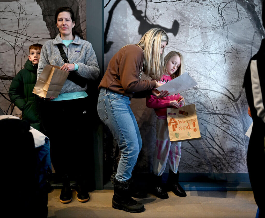 Bryn Hilts of Acton and her daughter Winnie, 8, right, wait in line to fill a bag of food for local children at the Acton Museum on Monday, January 20, 2025.  The Martin Luther King Day of Service activity was hosted by the Acton Museum Contemporary Leaders in partnership with Open Table. Ken McGagh/The Acton Bridge