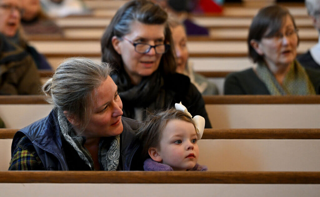 Alanna Widman of Acton and her daughter Mairi, 2, listen to the  Music Makes Me Happy Chorus sing a  Martin Luther King Day concert  at Trinitarian Congregational Church on Monday, January 20, 2025.  The chorus sang a series of spirituals and gospel songs including  “Go Down Moses,” “We Shall Overcome,” “Swing Low, Sweet Chariot,”  “Michael, Row the Boat Ashore,” “Wade in the Water,” “This Little Light of Mine,” and “When the Saints Go Marching In.”    Ken McGagh/The Acton Bridge