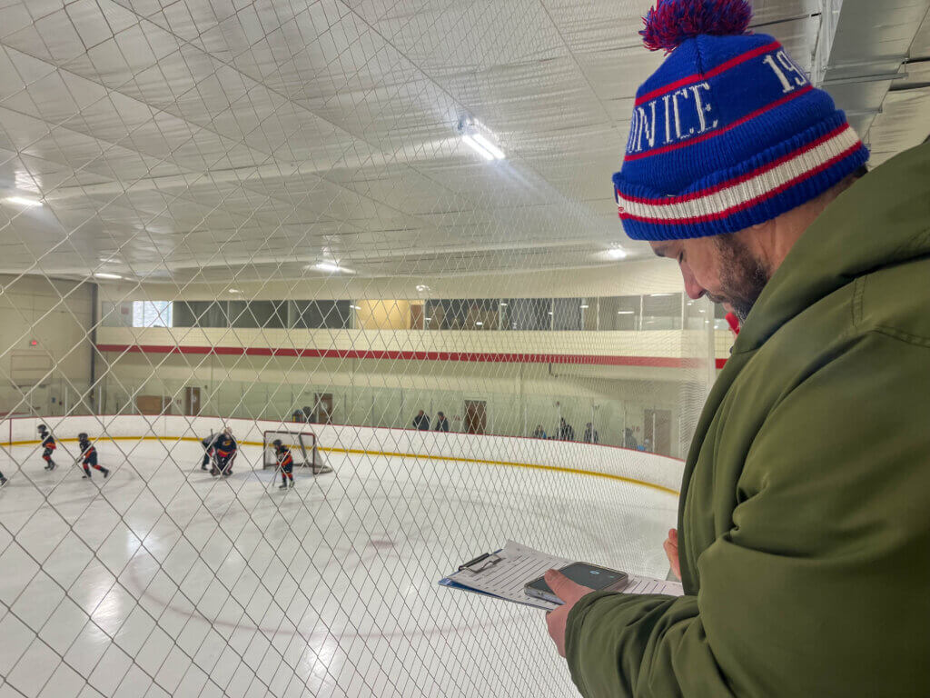 Chris Gaffron, phone and pen ready, captures team stats and Milan’s plays on the ice. Photo by Andrew Reed