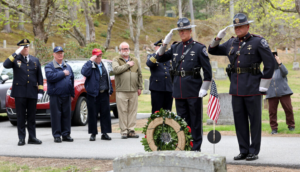 Concordian Peter Robinson, 79, in red hat, joins his brother, Bob Robinson, 86, of Wells, Maine, second from left, and nephew Mark Robinson of Mystic, Connecticut, and officers from the Middlesex Sheriffs Office in a salute during a flag placement ceremony in honor of his uncle, Jail Master David S. Robinson, at Sleepy Hollow Cemetery in Acton on Wednesday, April 29, 2026. A native of Acton, Jail Master Robinson was killed while attempting to prevent an escape at the Middlesex Jail in Cambridge on Mother’s Day, May 14, 1961. Ken McGagh/The Acton Bridge