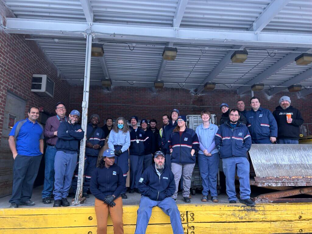 Postal workers, who ensure that The Bridge is safely delivered across Acton, pause on the dock 
of the Walden Street office before starting their rounds. Photo: Maile Hulihan/The Acton Bridge