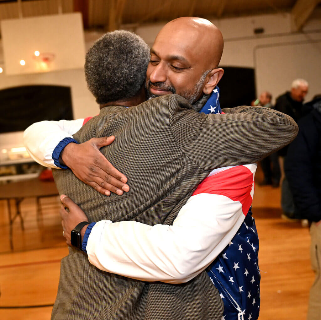 Sandeep Pisharody, right, hugs Michael Williams after winning seats on the School Committee and defeating an incumbent during a an election night unity rally at the Acton Armory on Tuesday, April 8, 2025. Ken McGagh/The Acton Bridge
