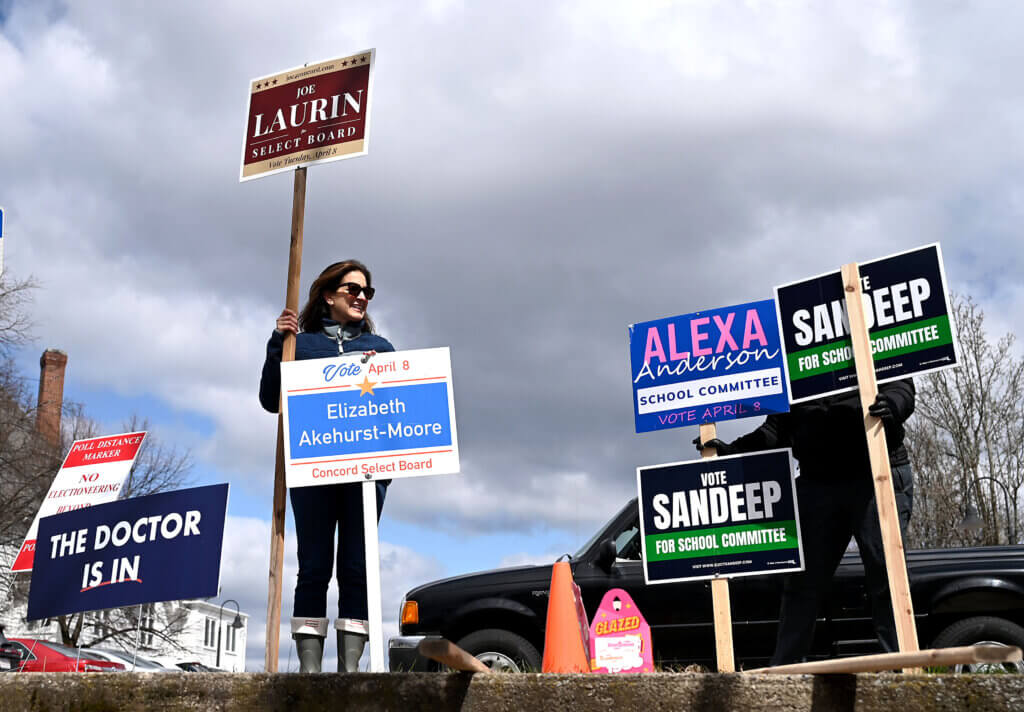 Martha McKennitt, center, holds signs in support of Select Board candidates Joe Laurin and Elizabeth Akehurst-Moore at the Harvey Wheeler Center polling place on Tuesday, April 8, 2025. Voters are deciding on two open seats on the Select Board and two open seats on the School Committee. Ken McGagh/The Acton Bridge