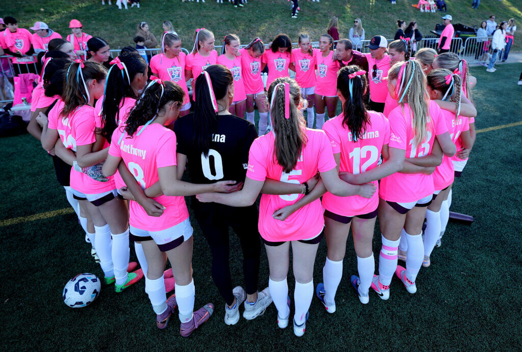 The Acton-Carlisle girls soccer team huddles before taking on Lincoln-Sudbury. Players wore the names of friends or family members who have battled cancer.
