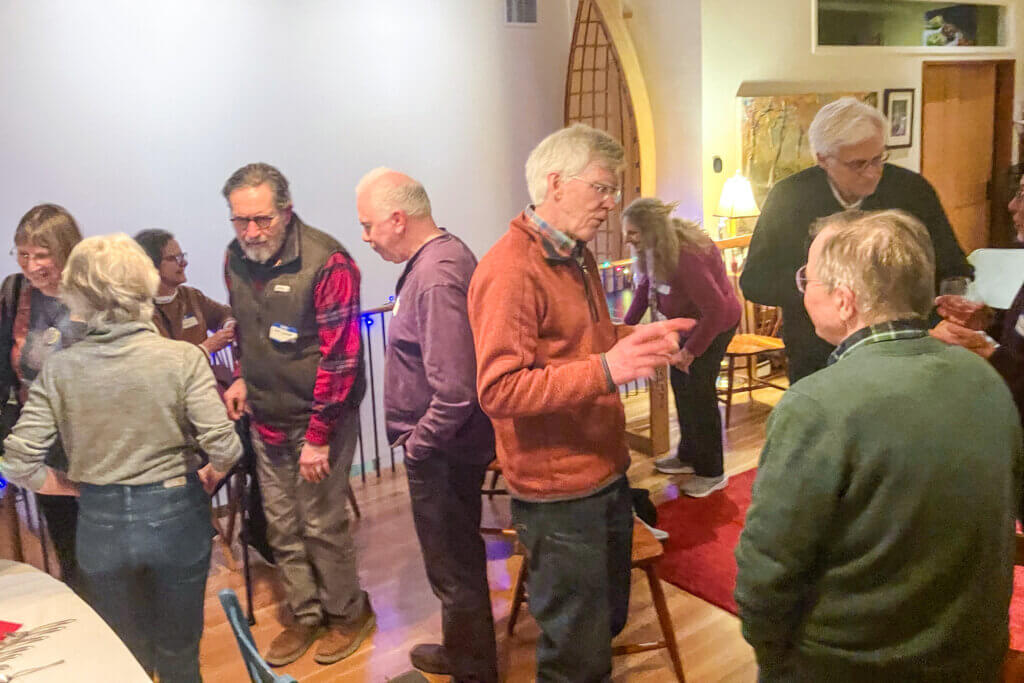 Select Board candidate Dean Banfield, in orange pullover, speaks with a voter while others mingle after a mid-February campaign event. Photo: Dakota Antelman/The Acton Bridge