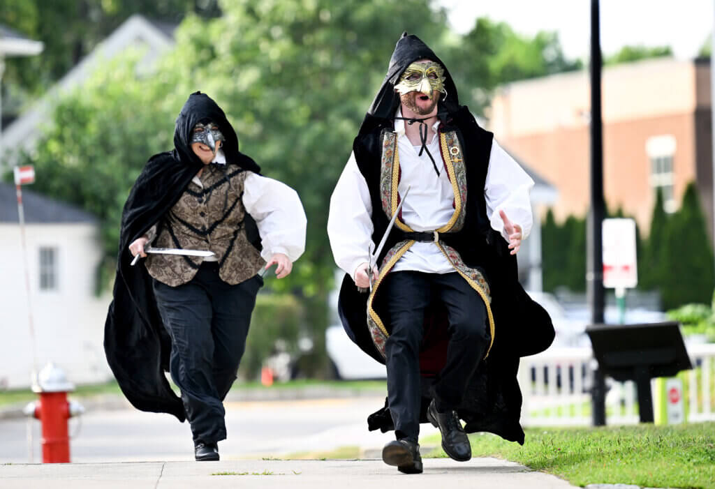 A pair of sword-bearing Acton Players actors sneak up the sidewalk during The World’s A Stage Players production of William Shakespeare’s “Henry IV, Part I” on the Acton Free Public Library lawn on Saturday, July 26, 2025. Ken McGagh/The Acton Bridge