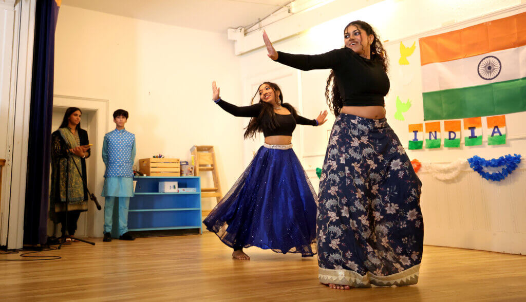 Prisha Rachakatla, 19, right, a rising college sophomore, and rising college freshman Neha Joshil, 18, dance a medley of Bollywood songs as master of ceremonies Maya, 17, and Shaan, 14, Soto look on during Acton's second annual India Day celebration at First Parish on August 16, 2025, Ken McGagh/The Acton Bridge