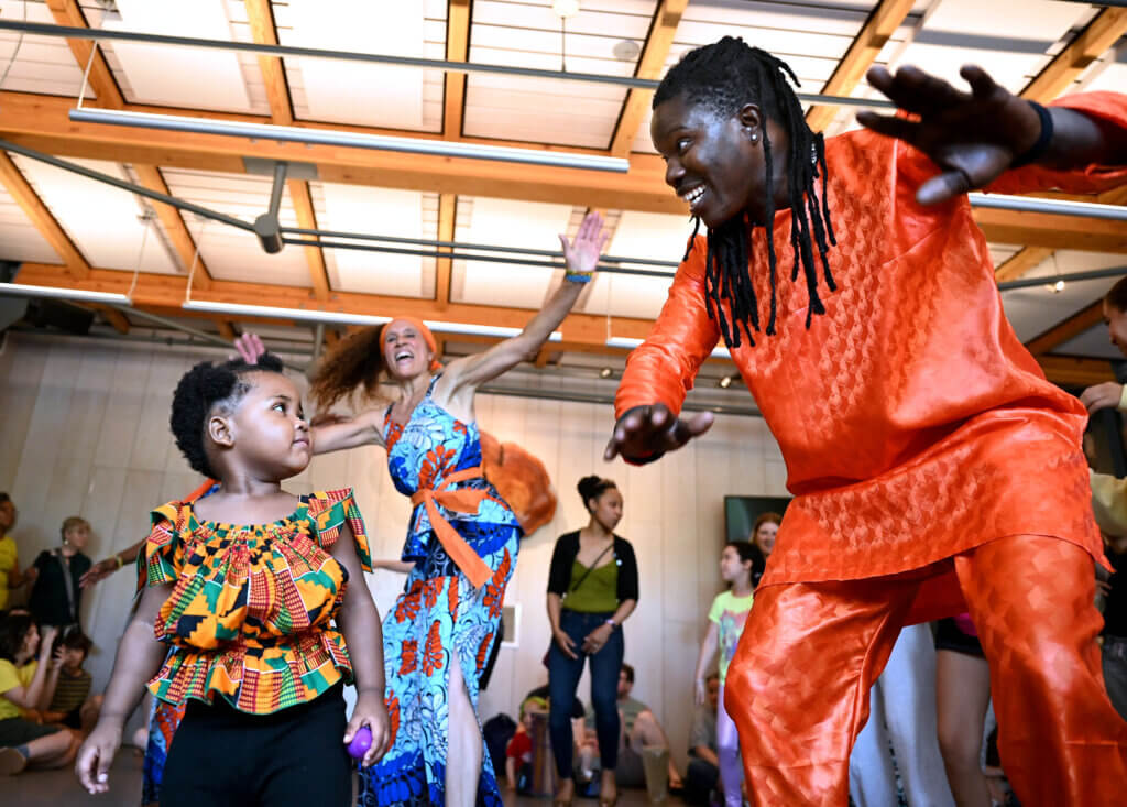 Namarie Charles, 2, of Acton, makes eye contact with dancer Aziz Mbengue of Ammaya Dance & Drum during a performance of traditional West African rhythm and movements at the Acton Museum’s Juneteenth family program on June 19. Namarie is the niece of Scynthia Charles, a dancer in the group. Photos: Ken McGagh/The Acton Bridge