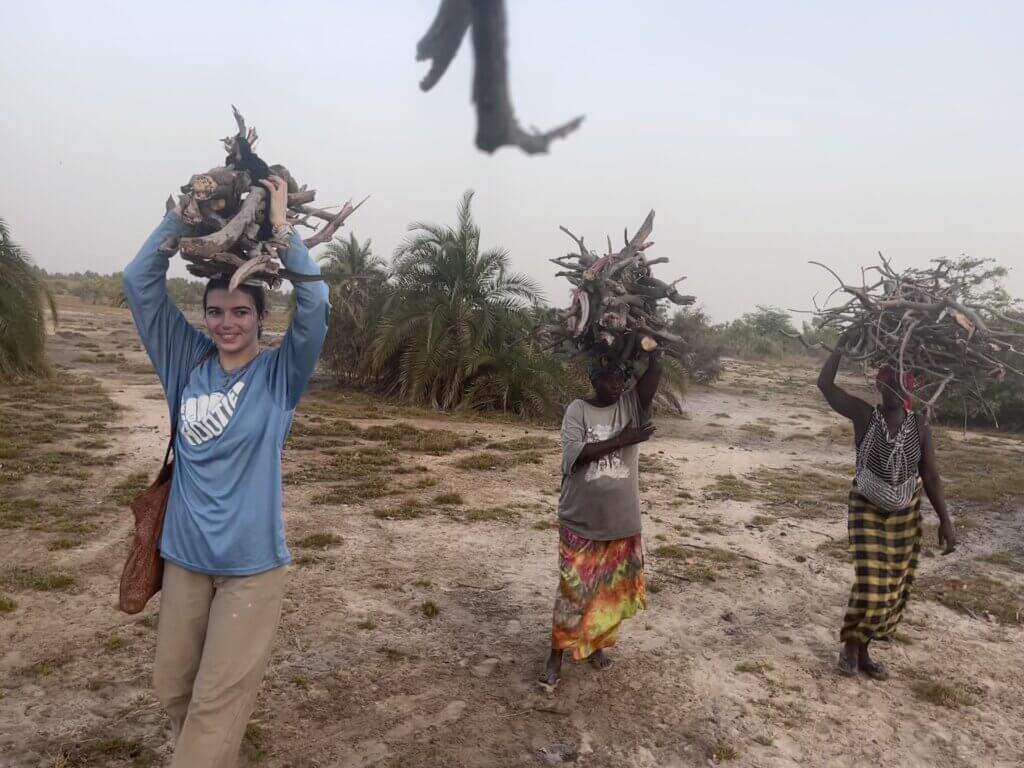 Mikaela Smith, left, beginning her eighth month of Peace Corps service, gathers firewood with her host mother and a neighbor in their Gambian village. Photo by Isatou Jobe