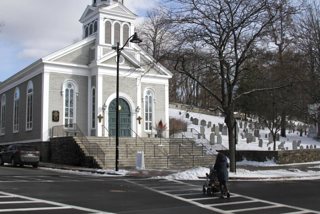 A person pushes a stroller across Monument Square in front of Acton’s Holy Family Parish. Photo: Dakota Antelman/The Acton Bridge