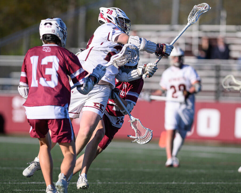 Acton-Carlisle’s James Reynolds (No. 28) scores the game-winning goal in overtime defended by Westford Academy’s Chase Boynton (No. 13) and Samuel Bramanti (24) defending on May 7. Photo by Jon Straggas