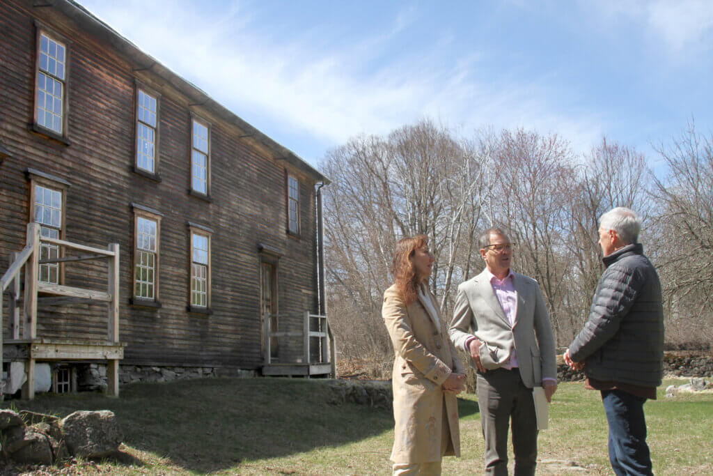 Save Our Heritage non-profit leaders Anna and Neil Rasmussen speak with Concord250 Executive Committee co-chair Gary Clayton in the shadow of the historic Barrett House. Photo: Dakota Antelman/The Acton Bridge