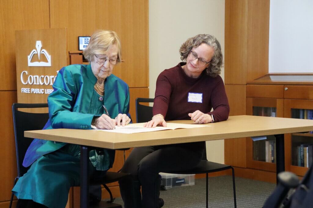 Susan Curtin, left, signed the paperwork presenting her late husband’s awards to the town archives on February 27 with Select Board Clerk Wendy Rovelli accepting the donation on behalf of the town. Photo: Trace Salzbrenner/The Acton Bridge