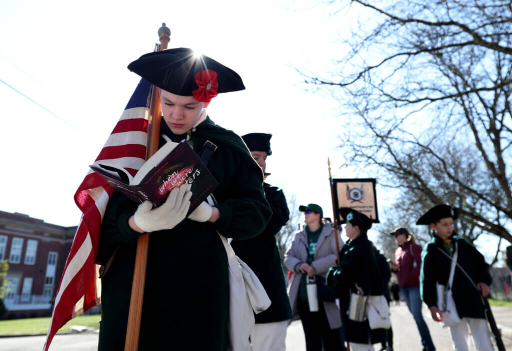 Kiera Jalandoni, 13, of the Middlesex County Fife and Drum Corps reads a novel as she and others wait in the early morning for the parade to begin.  
