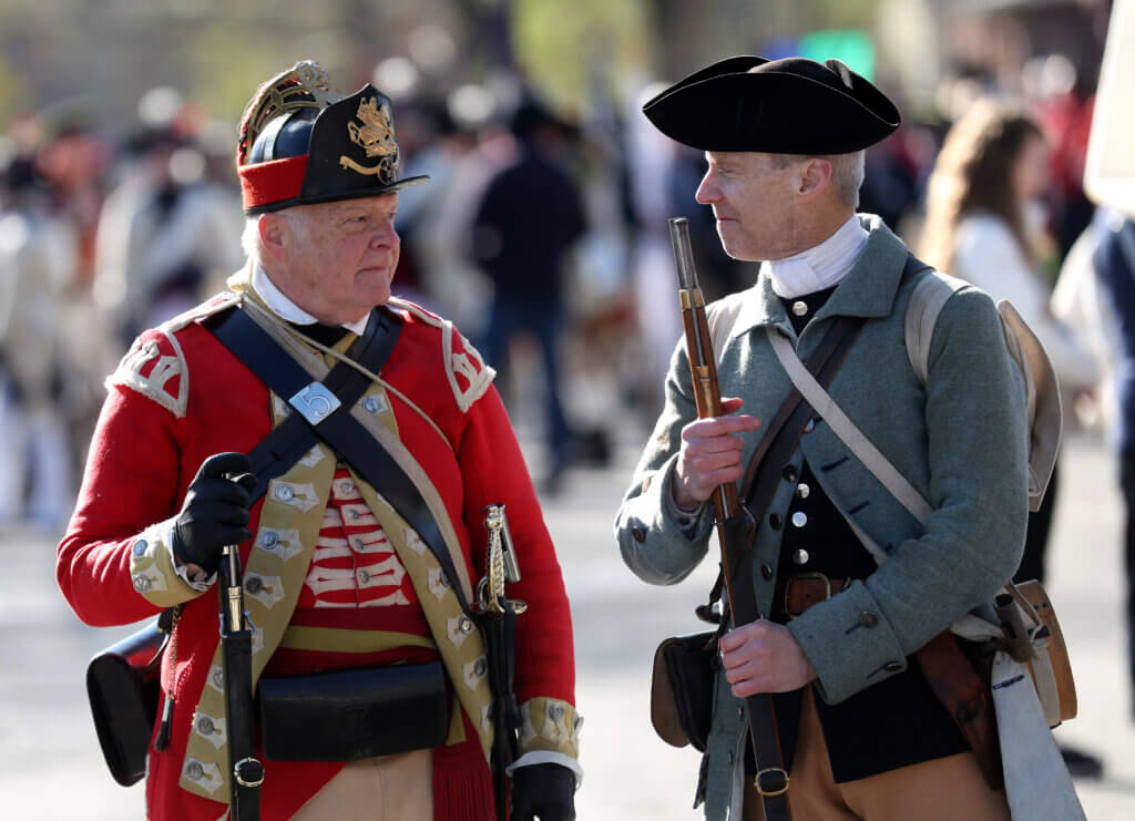 British and Colonial reenactors Steve Purington, left, of the Fifth Regiment of Foot, and Dave Thompson of the Acton Minutemen size each other up as participants stage on Stow Street before the parade.  
