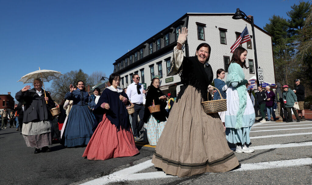 Jan Turnquist as Louisa May Alcott, center, and others from Orchard House wave to parade spectators. 
