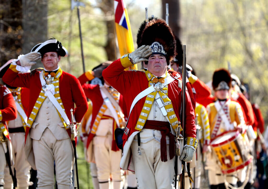 Reenactors clad as British officers offer a salute. 
