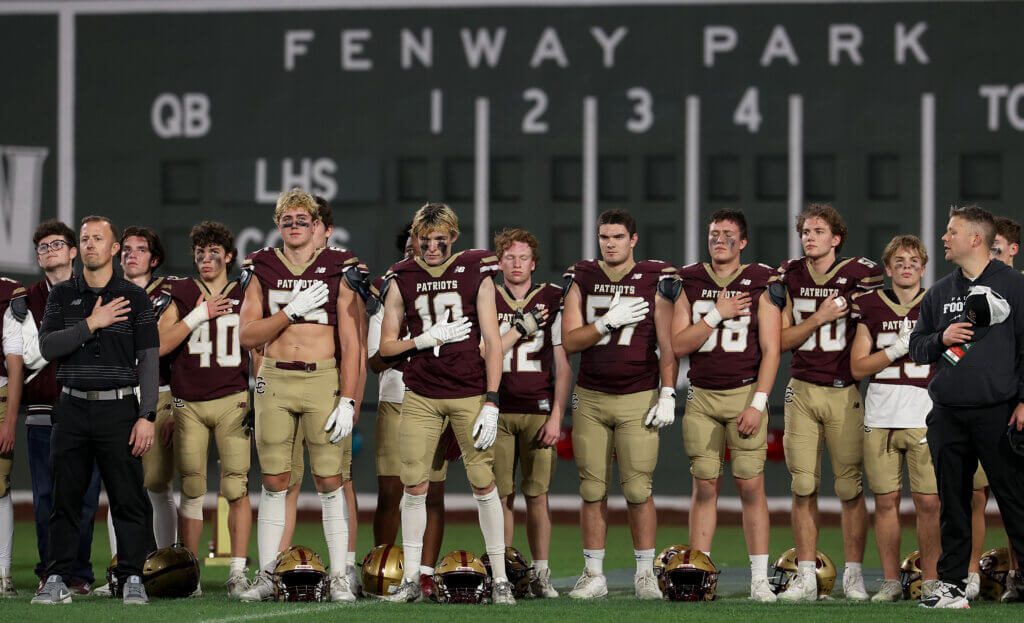 The Acton-Carlisle Patriots football team stands for the national anthem before the Thanksgiving Eve rivalry game against Lexington at Fenway Park on Wednesday, November 25, 2025. Ken McGagh/The Acton Bridge