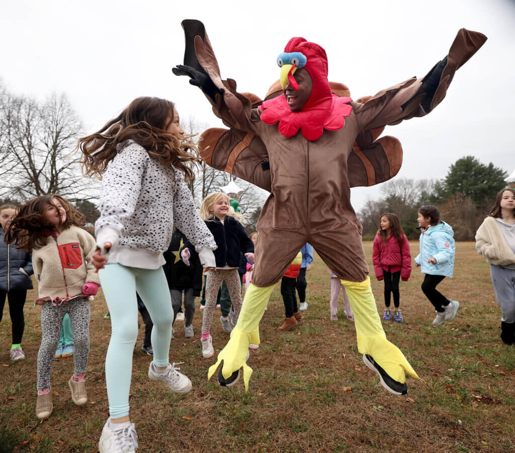 Physical education teacher Dave Corbett leads students in warmups during the Willard Elementary School’s annual Turkey Trot on Friday, November 21, 2025. The school’s Parent Teacher Group provided two turkey outfits and served as chaperones for the race. Ken McGagh/The Acton Bridge