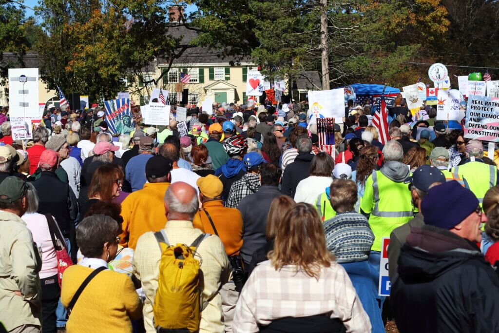 The crowd holds up their signs, facing historic Buttrick Mansion, as they listen to state Rep. Simon Cataldo (D-Acton). Photo: Trace Salzbrenner/The Acton Bridge