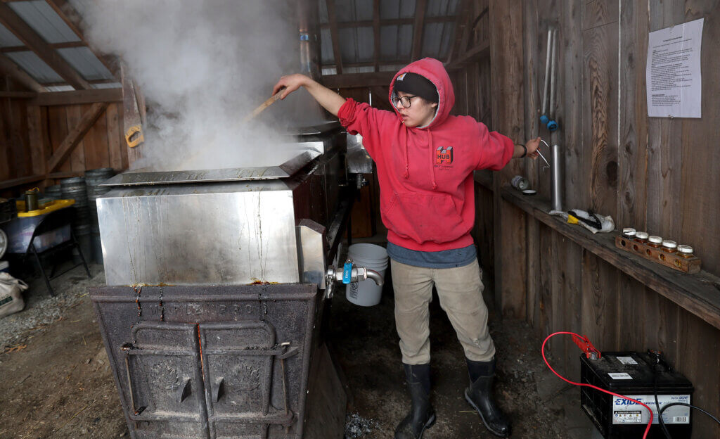 Ava Lublin, an assistant grower at Gaining Ground farm, stirs sap in the evaporator on Saturday, March 5, 2026.  Ken McGagh for The Acton Bridge