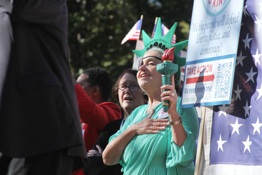 No Kings organizer Kate Kavanagh listens to the national anthem in her Statue of Liberty costume. Photo: Dakota Antelman/The Acton Bridge