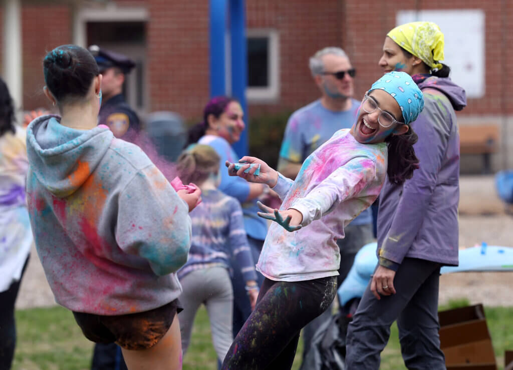 Maya Soto, 18, right, a member of the South Asian Student Society at Acton-Carlisle High School, douses a friend in colored powder during a Holi Celebration at the Alcott Eleme ntary School playground on Saturday, May 2, 2026. Ken McGagh/The Acton Bridge