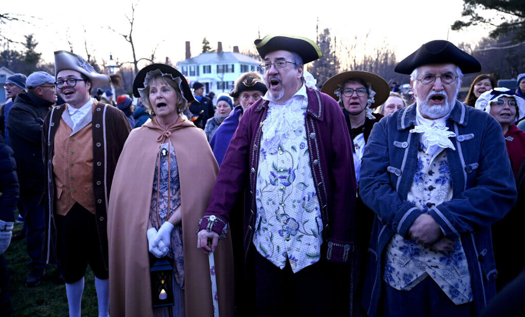 Members of the Acton Players sing as onlookers wait for the the arrival of cyclists from Boston. Photo: Ken McGagh/The Acton Bridge
