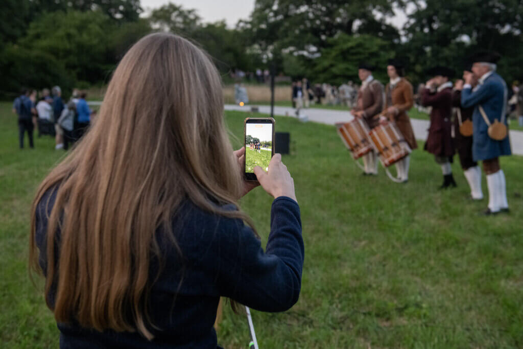 A woman takes a photo on her phone. Minute Man National Historical Park, cannon firing in honor of the Declaration of Independence. Jon Chase photo