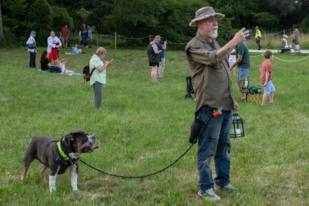 Mike Shook takes a photo with his dog Obi by his side. Minute Man National Historical Park, cannon firing in honor of the Declaration of Independence. Jon Chase photo