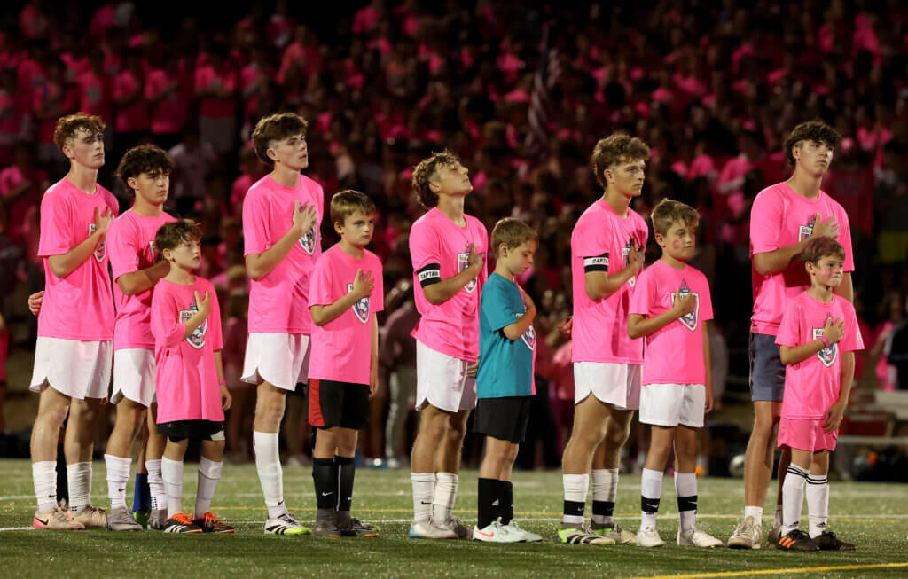 Boys in the Acton-Carlisle Youth Soccer program and CC varsity players stand for the national anthem before the climactic final match.
