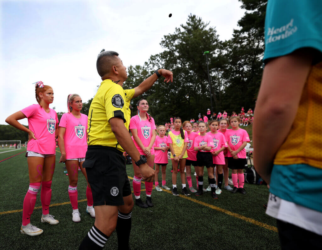 Acton-Carlisle girls soccer captains and girls in the Acton-Carlisle Youth Soccer program watch as a referee performs the opening coin toss for the match against Lincoln-Sudbury.
