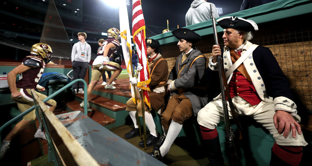 Acton Minute Men sit in the Red Sox dugout as the Patriots football players take the field for the second half.

